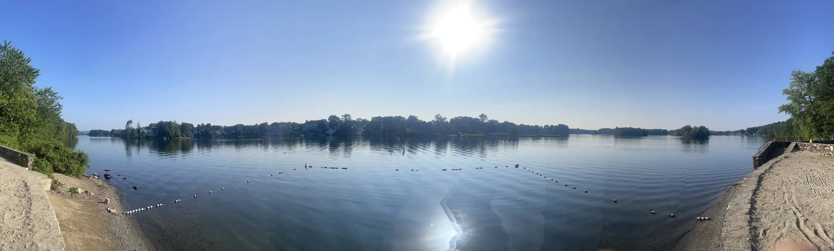 The sun above a calm lake with a wooded far shore